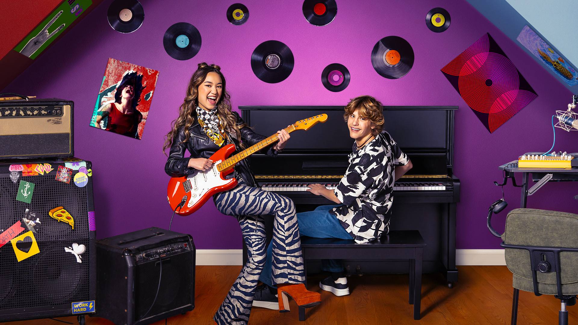 Erin, played by Ava Ro, plays a red guitar wearing black and white zebra pants and red shoes.  Aaron, played by Jensen Gering sits playing the piano.